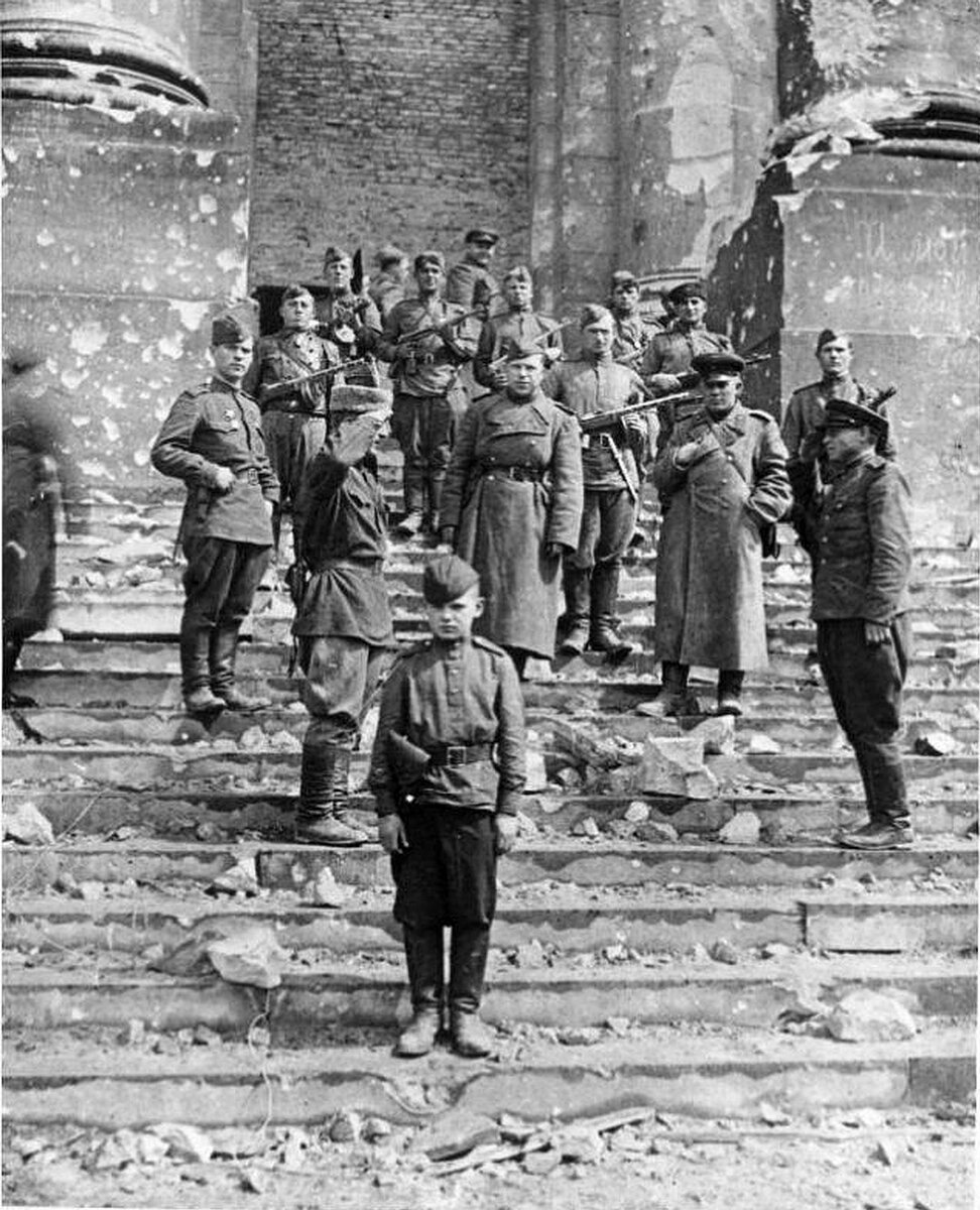 На фота байцы 150-й Ідрыцка-Бярлінскай ордэна Кутузава стралковай дывізіі на прыступках рэйхстага. На пярэднім плане Георгій Арцёменкаў (Берлін, май 1945 г.).Фота з асабістага архіва Г.А. Арцёменкава. Крыніца ілюстрацыі: Гомельская праўда. – 2009. – №№ 102-103. – С. 3.